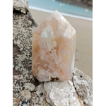 Pointe agate fleur de cerisier posée sur roche coquillée face à la plage, pierre rose crème naturelle, douceur émotionnelle et recentrage.