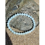Bracelet Aigue-Marine 6 mm sur sable près d’un rocher côtier, perles bleu tendre, calme mental et recentrage émotionnel.
