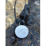 Pendentif rond œil de Sainte Lucie blanc sur lien noir, photographié sur roche sombre en extérieur, coquillage naturel associé à l’intuition et à la protection.