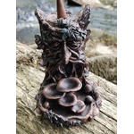 Brûleur d’encens à refoulement arbre en résine bronze posé sur mousse en forêt avec feuillage vert, visage sculpté et coupelles superposées pour effet cascade.