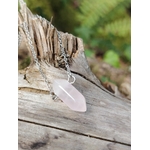 Pendentif pointe en quartz rose sur chaîne argentée posé sur bois brut fissuré, pierre rose délicate avec fond végétal flou, évoquant douceur relationnelle, rééquilibrage affectif et paix intérieure.
