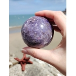 Sphère lépidolite tenue entre les doigts au bord de mer en Bretagne, pierre violette aux marbrures naturelles, apaisement du mental et recentrage.