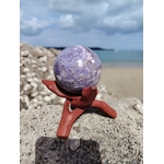 Sphère lépidolite photographiée sur rocher au bord de mer en Bretagne avec support en bois, pierre violette naturelle, sérénité intérieure et équilibre émotionnel.