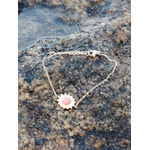 Bracelet fin doré avec soleil et rhodonite naturelle sur rocher coquillé face à la mer en Bretagne, acier inoxydable brillant et pierre rose tendre, charme délicat et énergie apaisante.