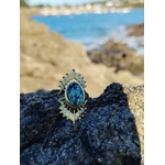 Bague dorée ajustable solaire avec pierre verte ovale sur rocher face à la mer en Bretagne, acier inoxydable brillant, énergie apaisante et allure élégante.