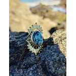 Bague solaire dorée ajustable avec pierre verte ovale sur roche côtière en Bretagne, acier inoxydable brillant et cabochon vert profond, style raffiné et équilibre émotionnel.