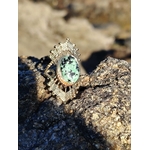 Bague solaire dorée en acier inoxydable sur roche marine en Bretagne, pierre verte ovale aux nuances profondes, élégance lumineuse et stabilité émotionnelle.