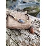 Bracelet labradorite facettée présenté sur bois naturel avec gland près d’un cours d’eau, médaillon ovale doré et cordon brun, recentrage et douceur intérieure.