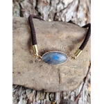Bracelet médaillon ovale facetté en labradorite sur pierre claire contre une écorce en forêt, cordon brun et monture dorée, intuition et protection subtile.