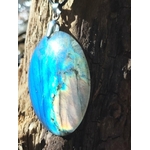 Pendentif ovale en labradorite aux reflets bleus sur roche au bord de mer en Bretagne, pierre naturelle à bélière argentée, protection énergétique et intuition.