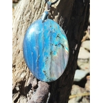 Pendentif ovale en labradorite photographié sur roche marine bretonne, éclats bleu lagon et vert doré sur pierre polie avec attache argentée, intuition éveillée et ancrage subtil.