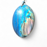 Pendentif ovale en labradorite sur fond blanc, pierre polie aux reflets bleu acier avec bélière argentée, allure minérale raffinée et énergie de recentrage.