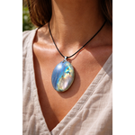 Pendentif ovale en labradorite bleue porté sur cordon noir, reflets bleu vert irisés sur peau en lumière naturelle, tenue beige et élégance protectrice.