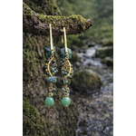 Boucles d’oreilles pendantes dorées avec pierres vertes style turquoise africaine suspendues sur branche moussue au bord d’un ruisseau, esprit bohème chic et élégance naturelle.