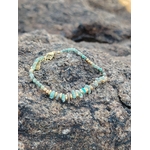 Zoom sur bracelet doré turquoise africaine et perles vert sauge sur roche naturelle en Bretagne, détails fins et teintes minérales, harmonie et apaisement intérieur.