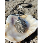 Pendentif pyrite naturelle sur coquillage blanc en extérieur en Bretagne, pierre ovale aux reflets métalliques avec cordon noir, symbole d’élan, de courage et de protection.