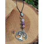 Bijou de téléphone arbre de vie en kunzite, lépidolite et rhodonite sur bois naturel avec feuillage en fond, création Magic Gaïa aux tons rose et mauve.