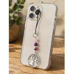 Bijou de téléphone arbre de vie avec kunzite, lépidolite et rhodonite accroché à une coque transparente sur support en bois, lumière naturelle et fond végétal flou.