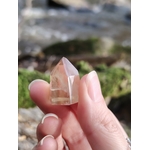 Pointe citrine naturelle tenue entre les doigts en lumière naturelle, petit cristal poli jaune clair, motivation, joie et vitalité.