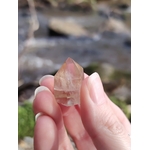 Pointe citrine naturelle entre les doigts en gros plan, petit cristal poli lumineux aux reflets dorés, bonne humeur, assurance et énergie solaire.