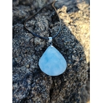 Pendentif calcite bleue naturelle présenté en extérieur sur bois brut en Bretagne, pierre goutte bleu laiteux, apaisement et équilibre émotionnel.