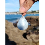 Pendentif calcite bleue naturelle posé sur bois en Bretagne avec arrière-plan de nature, pierre goutte bleu pastel, sérénité et lâcher-prise.