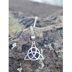 Pendentif Triquetra argent 925 en gros plan sur roche en Bretagne face à la mer, bijou celtique ajouré, ancrage, protection et stabilité intérieure.