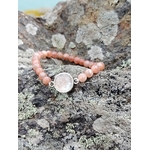 Gros plan bracelet Pierre de Soleil création Magic Gaïa sur rochers en Bretagne, perles rondes pêche rosé et support argenté, optimisme et assurance.
