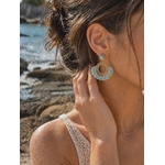 Boucle d’oreille dorée éventail tissé bleu turquoise portée à l’oreille face à la mer en Bretagne, élégance estivale