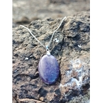 Pendentif Lépidolite ovale violette posé sur roche brute en Bretagne, pierre naturelle de calme intérieur, de transition douce et de bien-être émotionnel