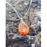 Pendentif Ambre baltique goutte sur roche sombre en Bretagne, reflets feu et miel, protection douce et chaleur réconfortante.