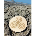Plaque en bois Triskell 10 cm posée sur rochers en Bretagne, symbole celtique d’équilibre et de cycles naturels.
