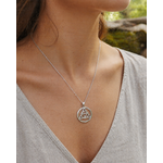 Pendentif Triquetra rond en argent 925 porté sur décolleté clair, collier celtique ajouré en lumière naturelle.