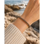 Bracelet Quartz fumé porté au poignet en Bretagne, décor marin flouté, perles brunes translucides pour ancrage et apaisement.