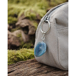 Porte-clés Fluorite multicolore en situation naturelle, accroché à un sac clair avec pierre verte et violette.