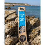 Encens AUM Organico Contre le Mauvais Œil 25 g posé sur roche en bord de mer breton, boîte kraft et bleue avec bâtonnets visibles.