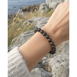 Bracelet bronzite porté au poignet en décor naturel breton, perles sombres et dorées pour ancrage, courage et protection symbolique.