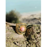 Bague dorée ajustable en acier inoxydable photographiée en Bretagne sur bois flotté, cabochon rose pour douceur et harmonie émotionnelle.