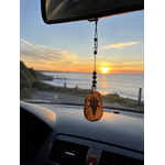 Bijou de rétroviseur Magic Gaïa suspendu dans une voiture face à la mer au coucher du soleil, symbole Gaïa pour voyager avec sérénité.