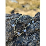 Gros plan du bracelet doré sur roche bretonne, maillons fins et perles violettes facettées pour une touche élégante.