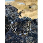 Bracelet doré posé sur pierre naturelle en bord de mer, perles violettes lumineuses pour élégance et sérénité.