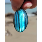 Labradorite bleue tenue devant la plage en Bretagne, pierre ovale brillante pour présence et perception subtile.