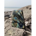 Labradorite polie dressée sur rochers bretons, mer floutée en arrière-plan pour intuition calme et énergie stable.