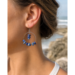 Boucle d’oreille Lapis-Lazuli création Magic Gaïa portée à l’oreille, fond marin flouté en Bretagne, chips bleues et acier inoxydable.