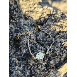 Bracelet Améthyste feuille dorée posé sur rocher coquillé en bord de mer, rallonge et médaillon visibles, perles violettes pour paix intérieure, méditation et sensibilité.