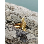 Bague fleur dorée réglable vue de profil sur rocher en bord de mer, anneau ajustable visible et fleur texturée en acier inoxydable.