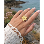 Bague fleur dorée réglable portée à la main près de la mer, acier inoxydable finition or 18K avec motif floral élégant et naturel.