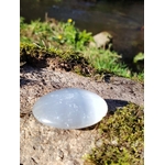 Galet Sélénite blanc poli posé sur rocher moussu près d’un ruisseau, pierre lumineuse pour purification douce et clarté intérieure.
