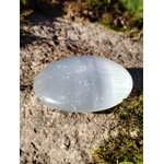 Galet Sélénite blanc laiteux sur pierre naturelle, forme ovale brillante avec fines stries visibles pour lumière et sérénité.