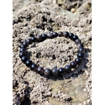 Bracelet Obsidienne Argentée posé sur roche texturée en Bretagne, perles foncées lumineuses pour soutenir les limites personnelles et la force intérieure.